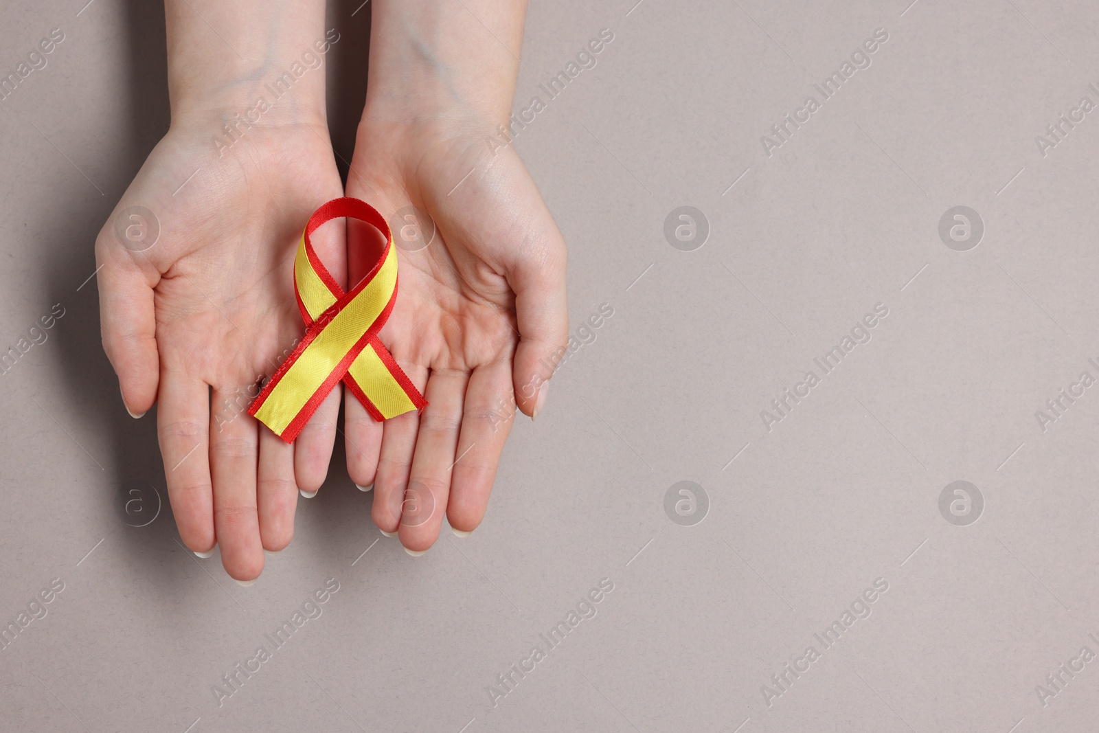 Photo of Woman with yellow and red ribbon on grey background, top view with space for text. Hepatitis C awareness