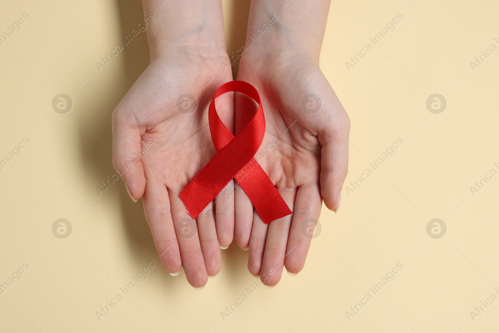 Photo of Woman with red ribbon on beige background, top view. HIV (AIDS) disease awareness