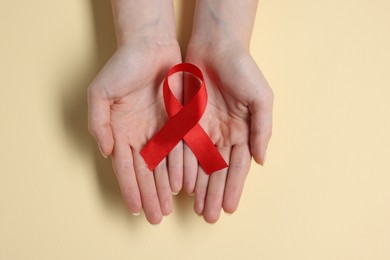 Photo of Woman with red ribbon on beige background, top view. HIV (AIDS) disease awareness