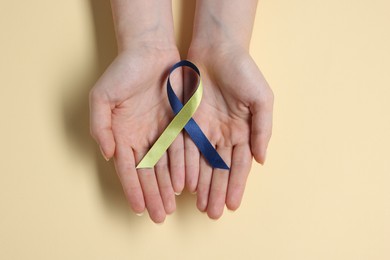 Woman with yellow and blue ribbon on beige background, top view. Down syndrome awareness