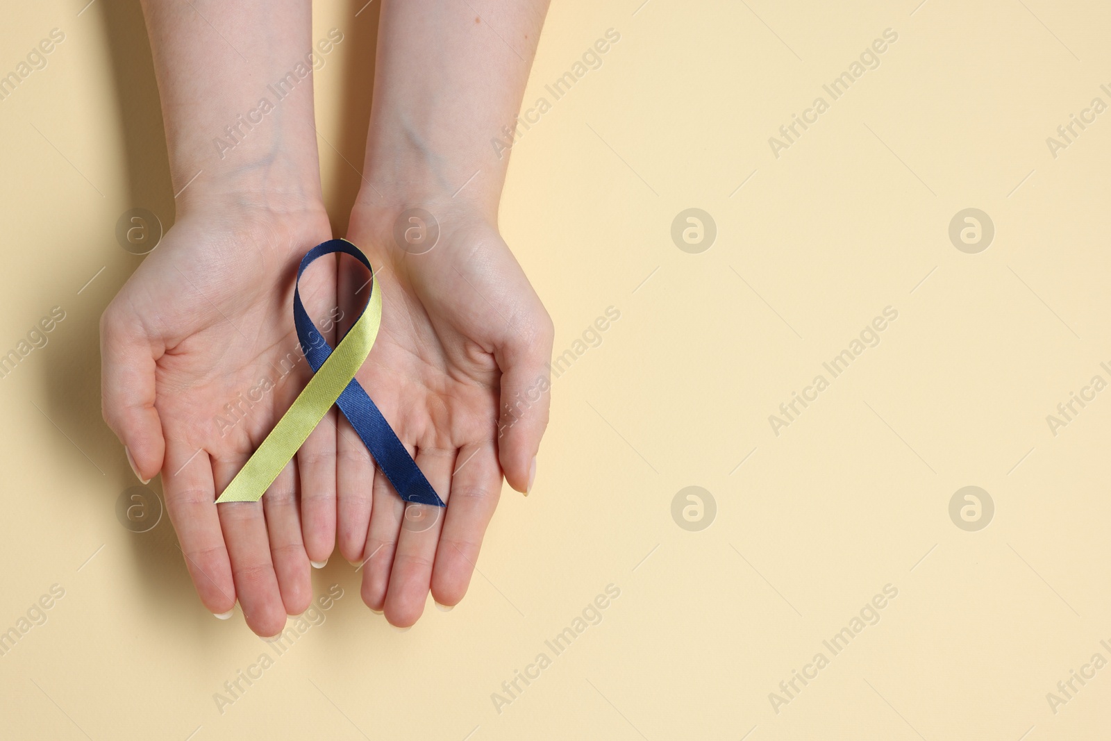 Photo of Woman with yellow and blue ribbon on beige background, top view with space for text. Down syndrome awareness