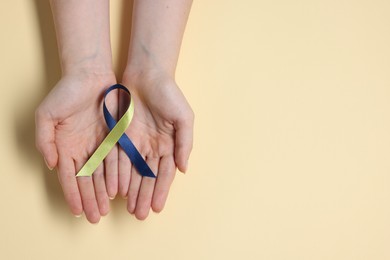 Photo of Woman with yellow and blue ribbon on beige background, top view with space for text. Down syndrome awareness