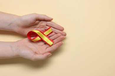 Photo of Woman with yellow and red ribbon on beige background, top view with space for text. Hepatitis C awareness