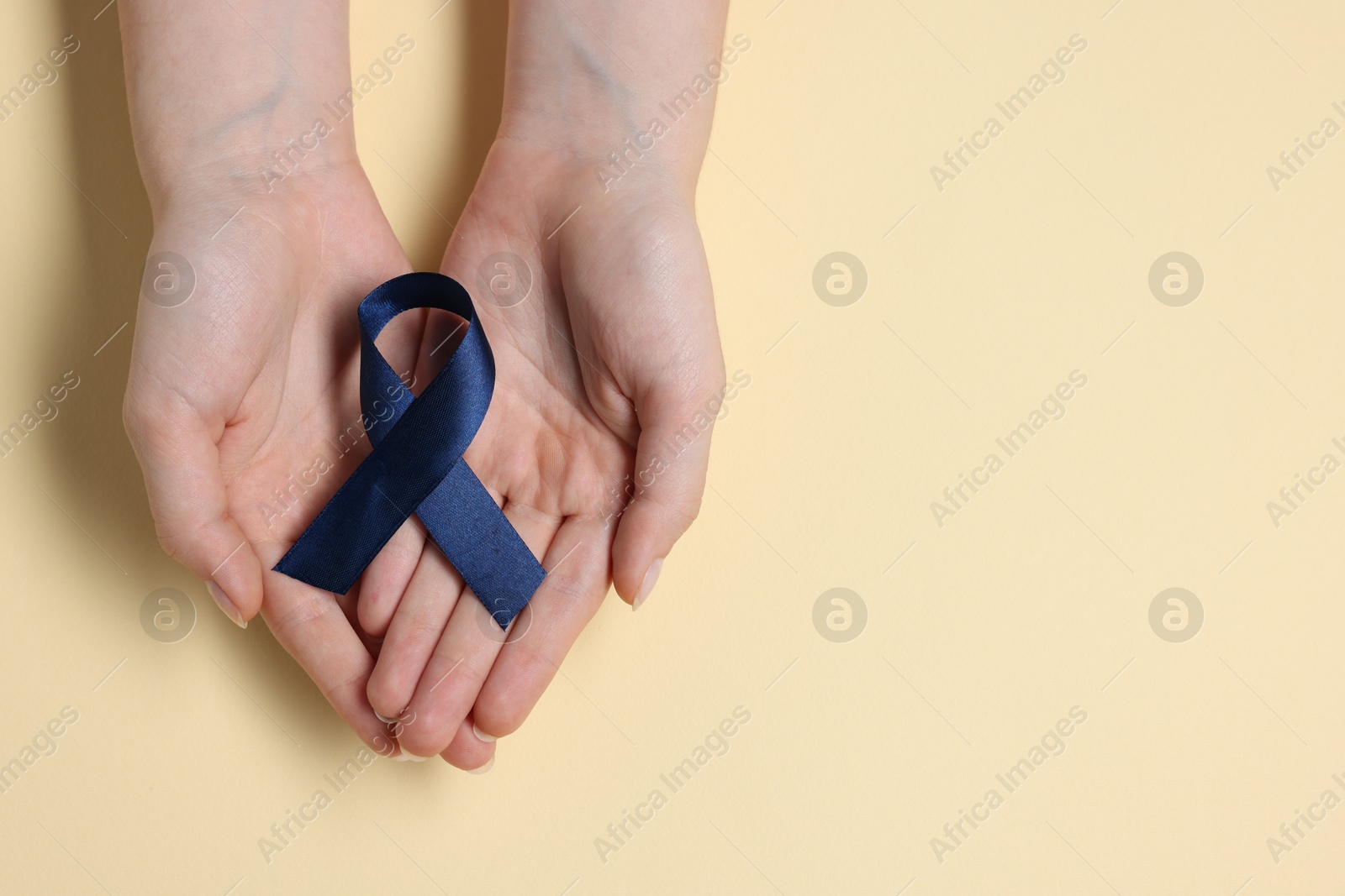 Photo of Woman with dark blue ribbon on beige background, top view with space for text. Arthritis disease and colon cancer awareness