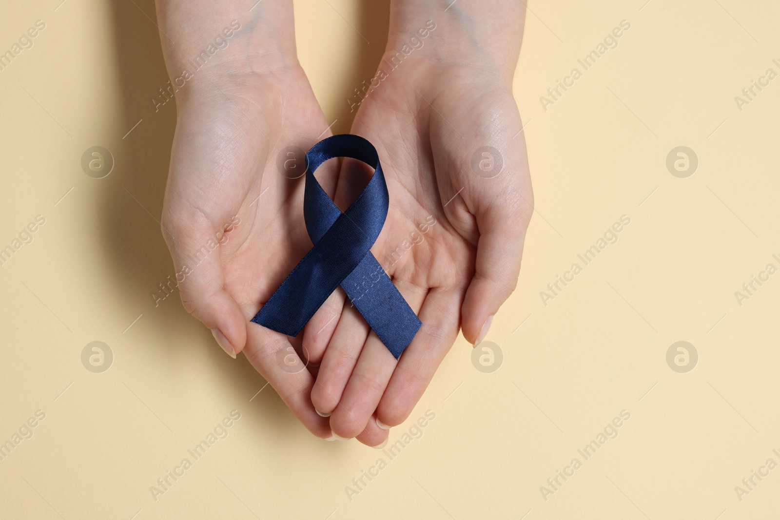 Photo of Woman with dark blue ribbon on beige background, top view. Arthritis disease and colon cancer awareness