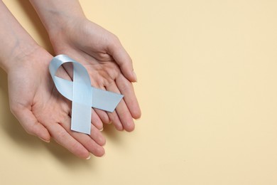 Photo of Woman with light blue ribbon on beige background, top view and space for text. Childhood cancer awareness