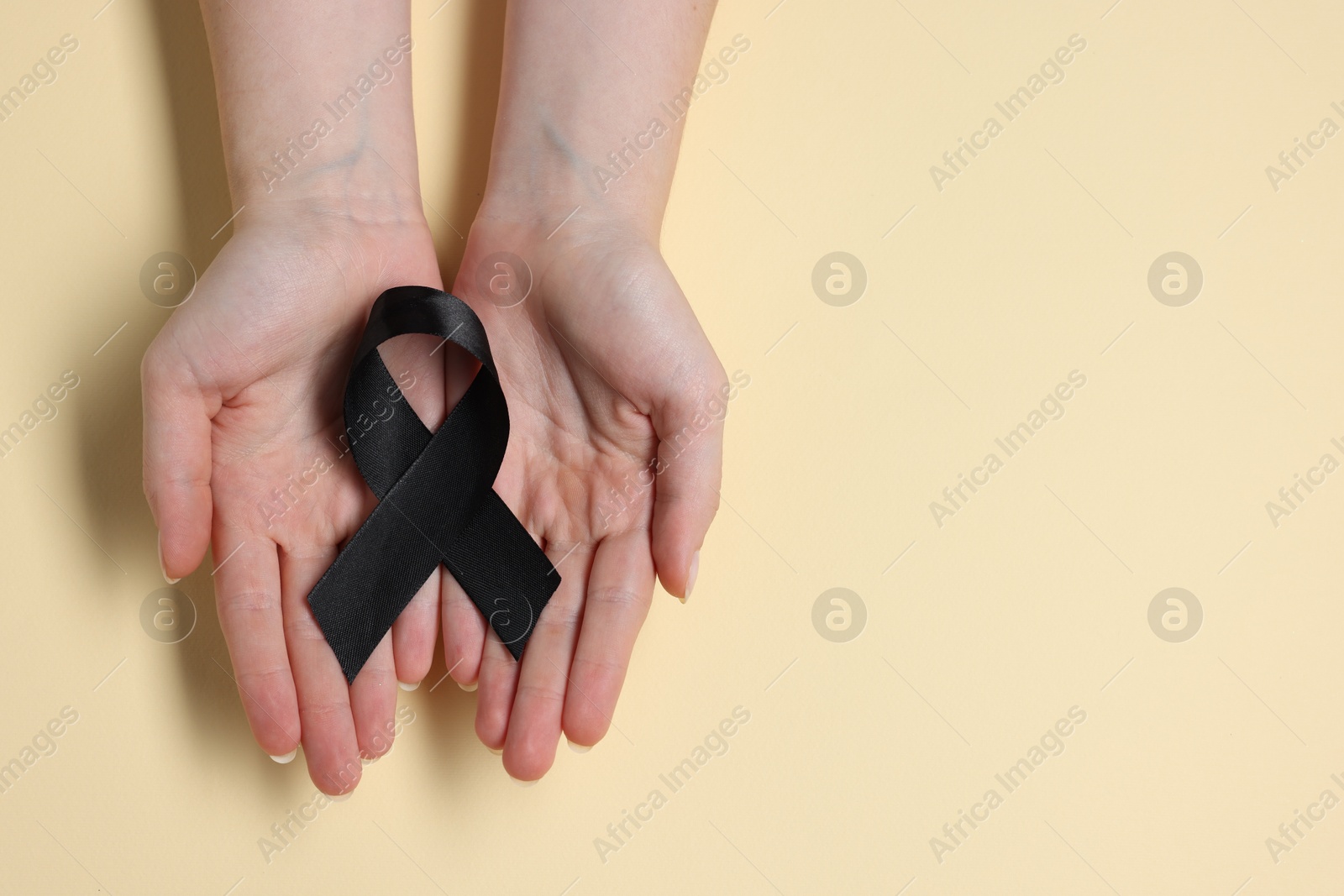 Photo of Woman with black ribbon on beige background, top view with space for text. Melanoma and mourning concept