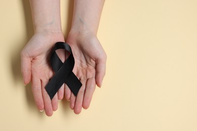 Photo of Woman with black ribbon on beige background, top view with space for text. Melanoma and mourning concept