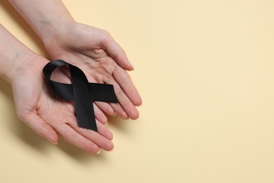 Photo of Woman with black ribbon on beige background, top view with space for text. Melanoma and mourning concept