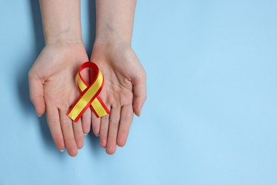 Photo of Woman with yellow and red ribbon on light blue background, top view with space for text. Hepatitis C awareness