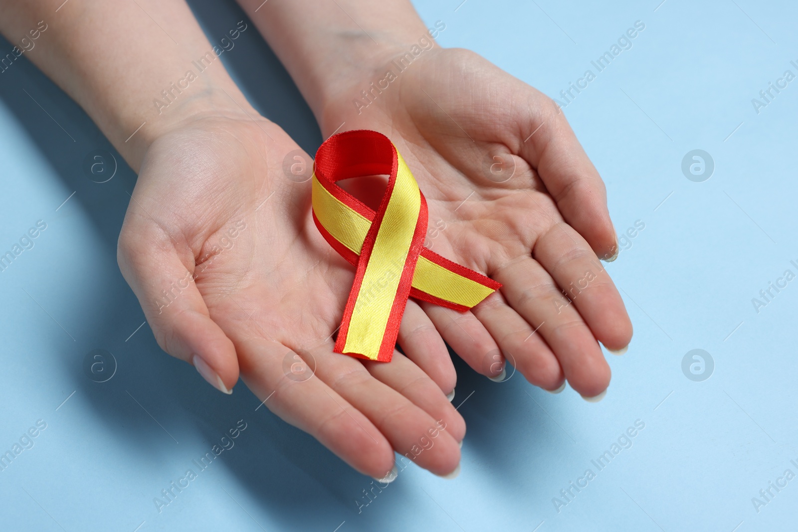 Photo of Woman with yellow and red ribbon on light blue background, closeup. Hepatitis C awareness