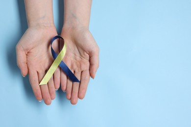 Photo of Woman with colorful ribbon on light blue background, top view and space for text. Down syndrome awareness