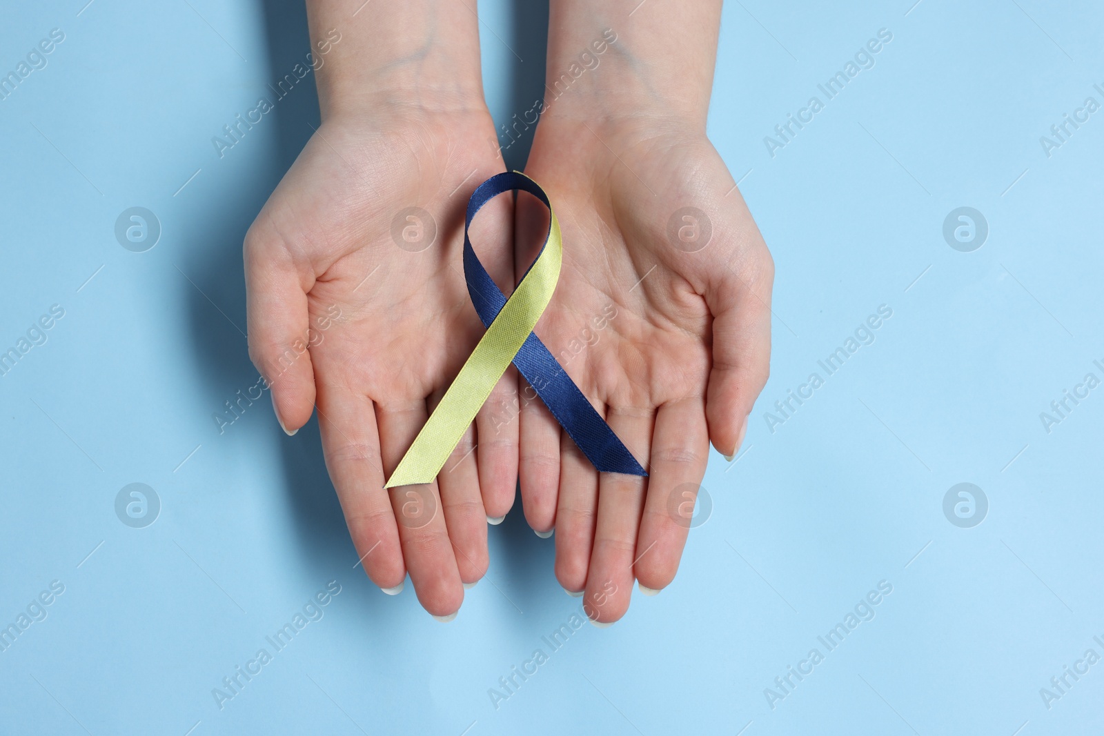 Photo of Woman with colorful ribbon on light blue background, top view. Down syndrome awareness