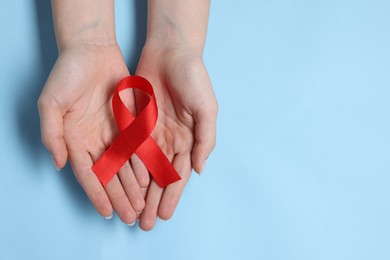 Photo of Woman with red ribbon on light blue background, top view and space for text. HIV (AIDS) disease awareness