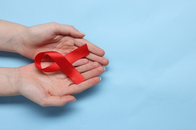 Photo of Woman with red ribbon on light blue background, top view and space for text. HIV (AIDS) disease awareness