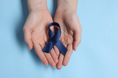 Photo of Woman with ribbon on light blue background, top view. Arthritis disease and colon cancer awareness