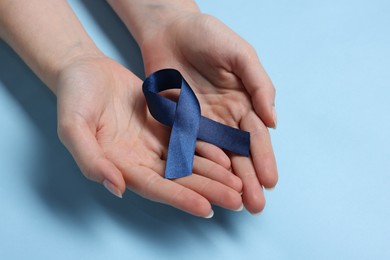 Photo of Woman with ribbon on light blue background, closeup. Arthritis disease and colon cancer awareness