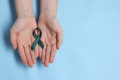 Photo of Woman with teal ribbon on light blue background, top view with space for text. Ovarian cancer and gynecological disorders awareness