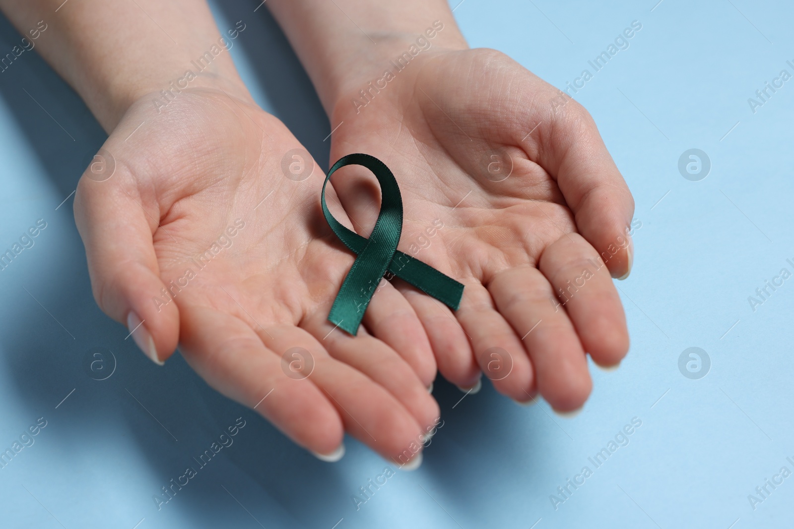 Photo of Woman with teal ribbon on light blue background, closeup. Ovarian cancer and gynecological disorders awareness