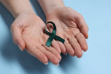 Photo of Woman with teal ribbon on light blue background, closeup. Ovarian cancer and gynecological disorders awareness