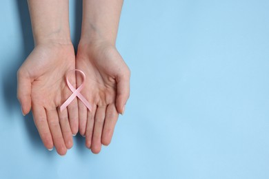 Photo of Woman with pink ribbon on light blue background, top view with space for text. Breast cancer awareness