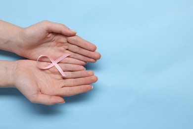 Photo of Woman with pink ribbon on light blue background, top view with space for text. Breast cancer awareness