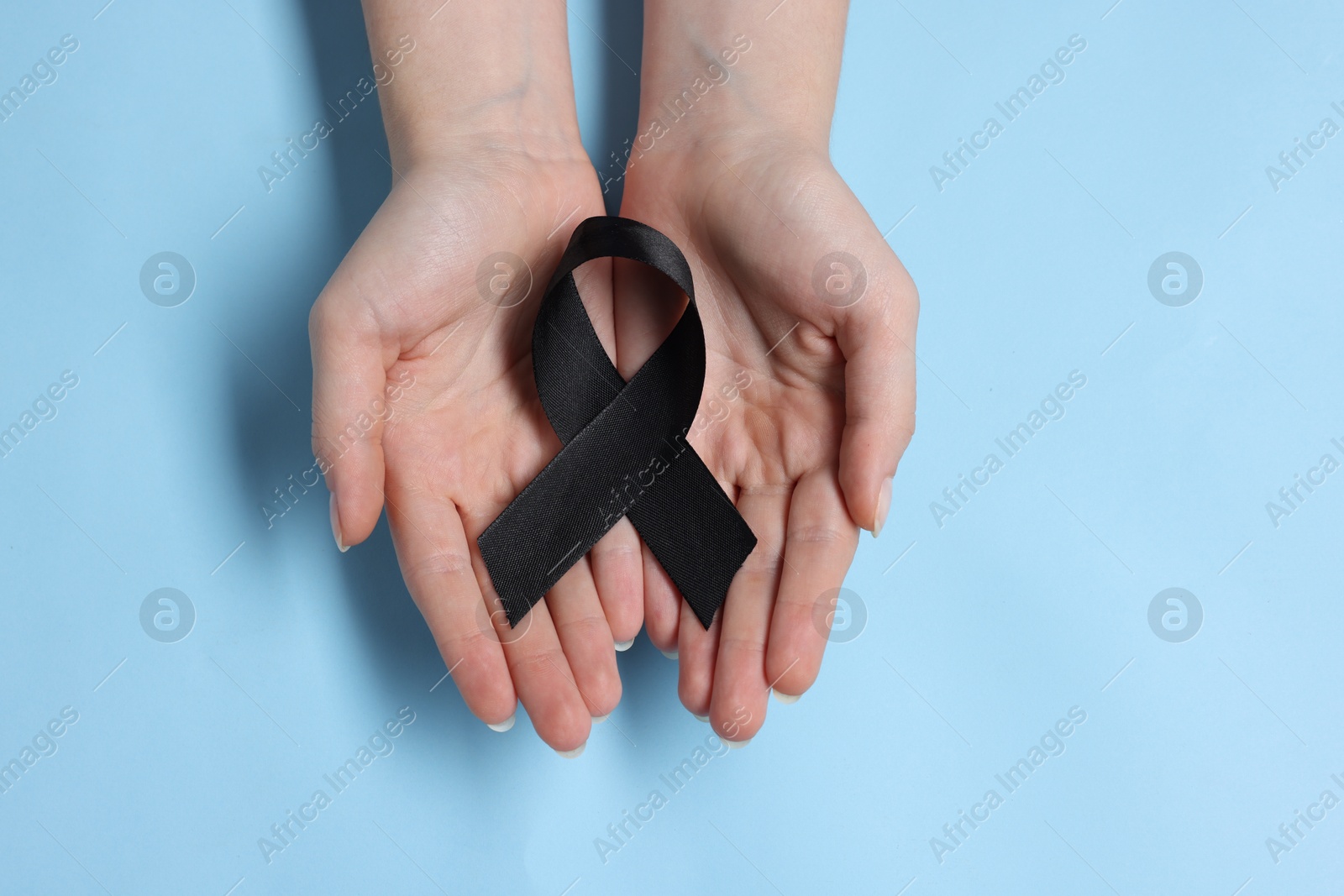 Photo of Woman with black ribbon on light blue background, top view. Melanoma and mourning concept