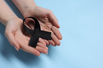 Photo of Woman with black ribbon on light blue background, closeup with space for text. Melanoma and mourning concept