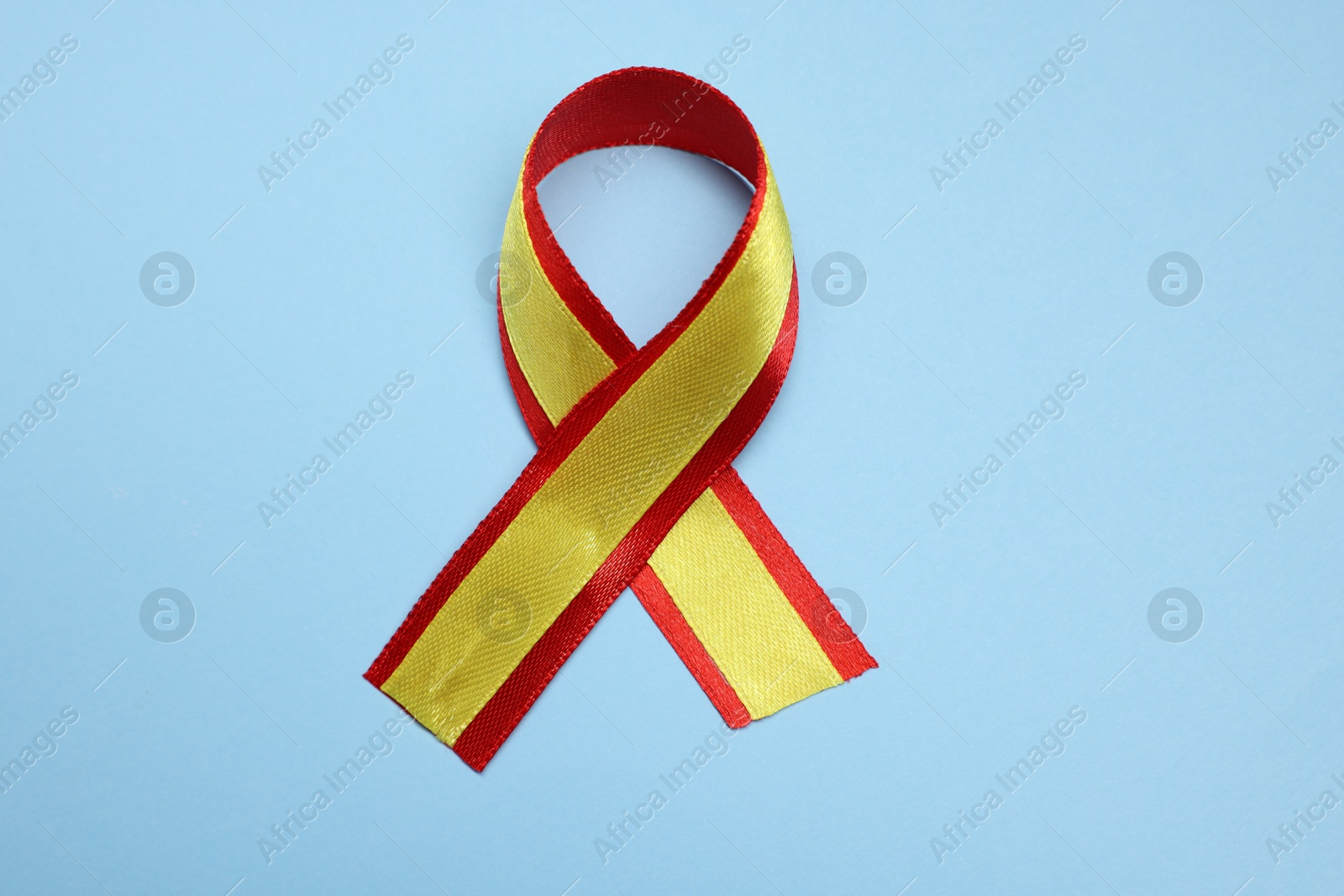 Photo of One yellow and red ribbon on light blue background, top view. Hepatitis C awareness