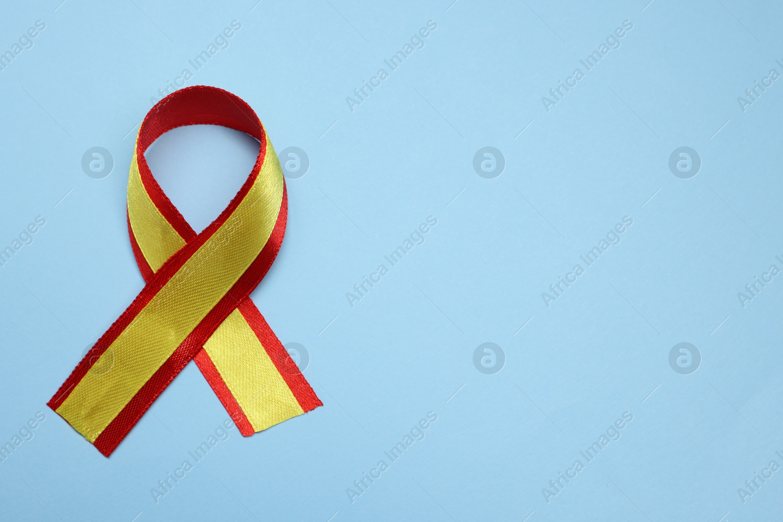 Photo of One yellow and red ribbon on light blue background, top view with space for text. Hepatitis C awareness