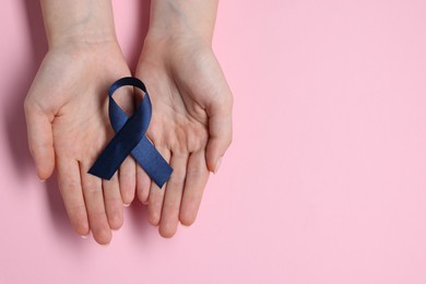 Photo of Woman with dark blue ribbon on pink background, top view with space for text. Arthritis disease and colon cancer awareness