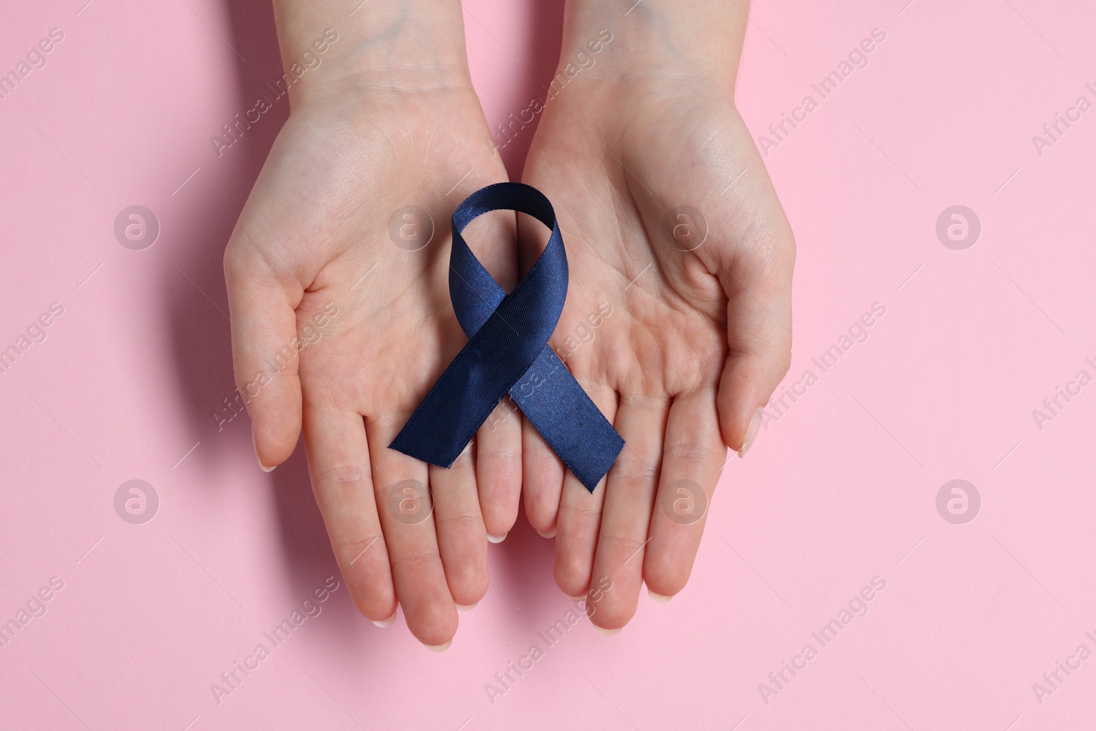 Photo of Woman with dark blue ribbon on pink background, top view. Arthritis disease and colon cancer awareness