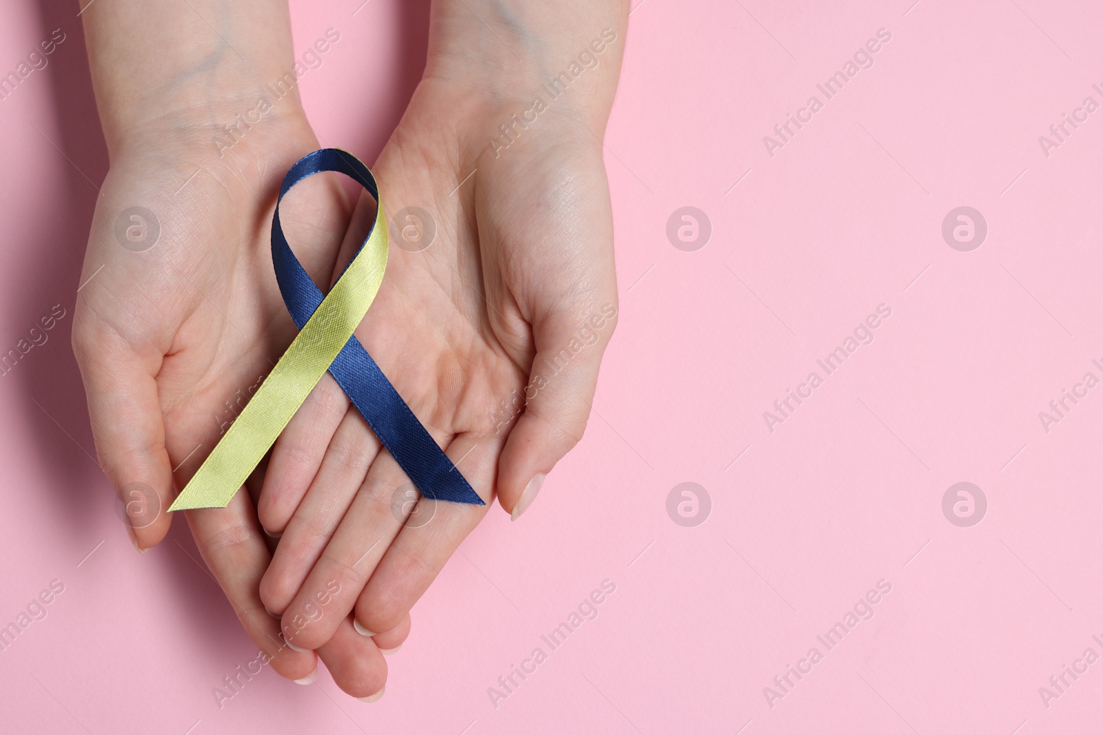 Photo of Woman with yellow and blue ribbon on pink background, top view with space for text. Down syndrome awareness