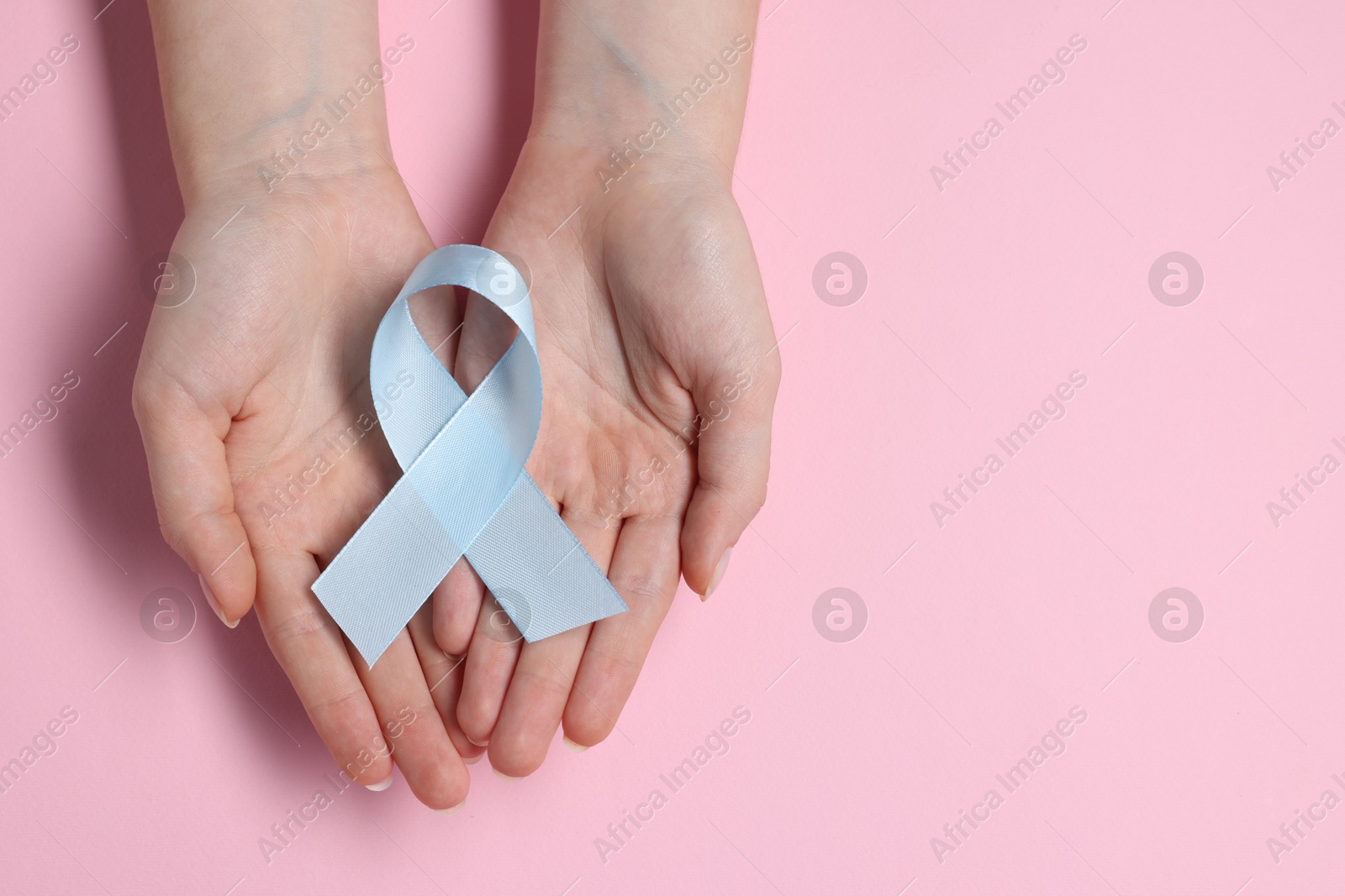 Photo of Woman with light blue ribbon on pink background, top view and space for text. Childhood cancer awareness