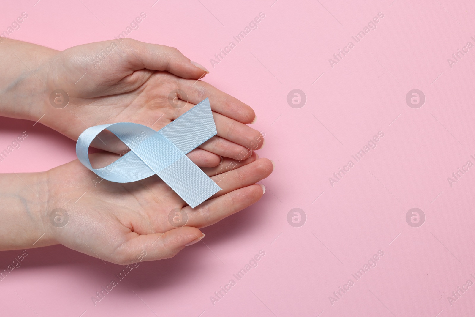 Photo of Woman with light blue ribbon on pink background, top view and space for text. Childhood cancer awareness