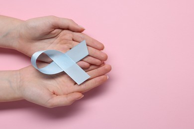 Woman with light blue ribbon on pink background, top view and space for text. Childhood cancer awareness