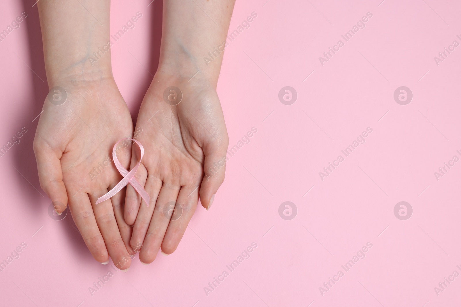 Photo of Woman with ribbon on pink background, top view and space for text. Breast cancer awareness