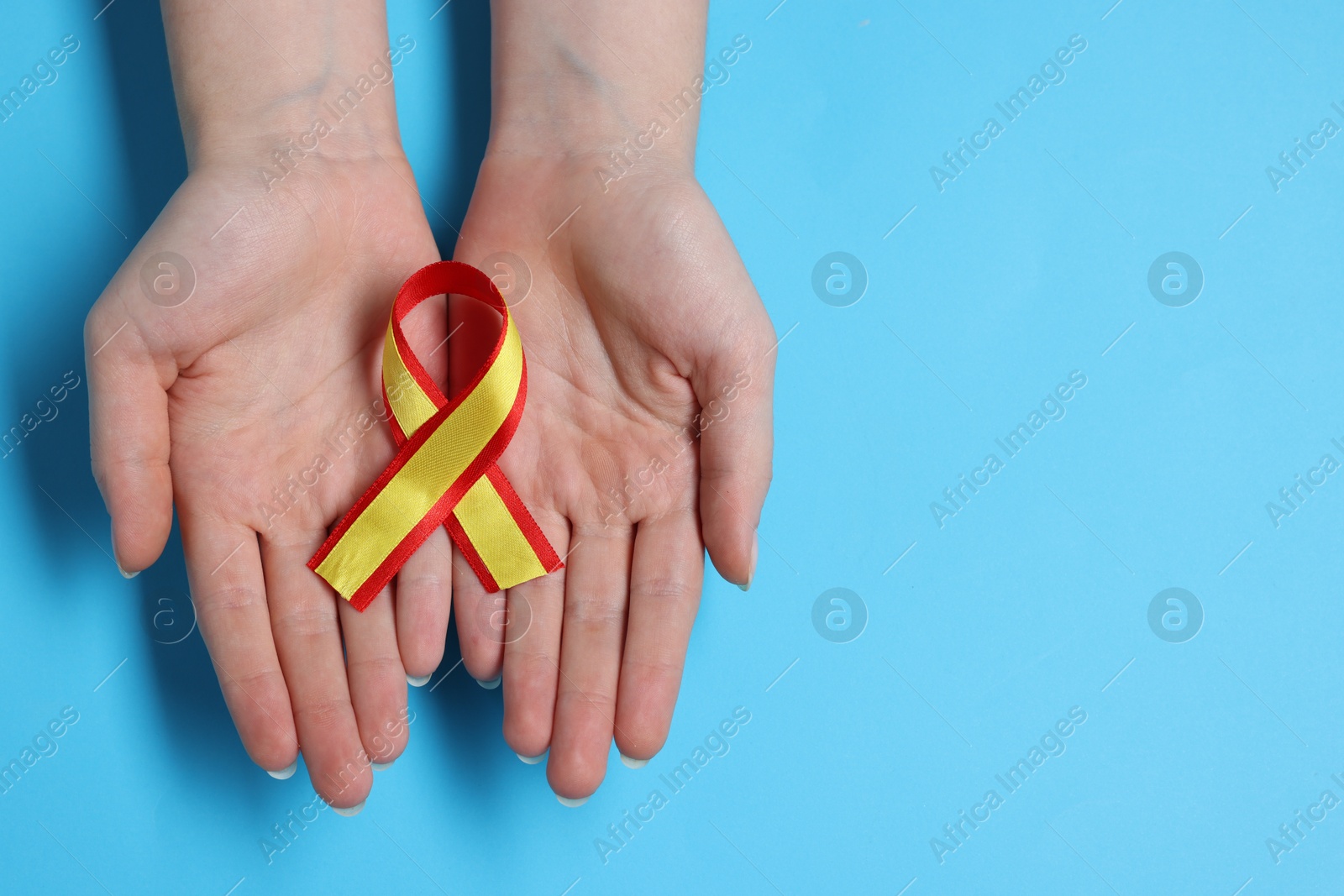 Photo of Woman with yellow and red ribbon on light blue background, top view with space for text. Hepatitis C awareness