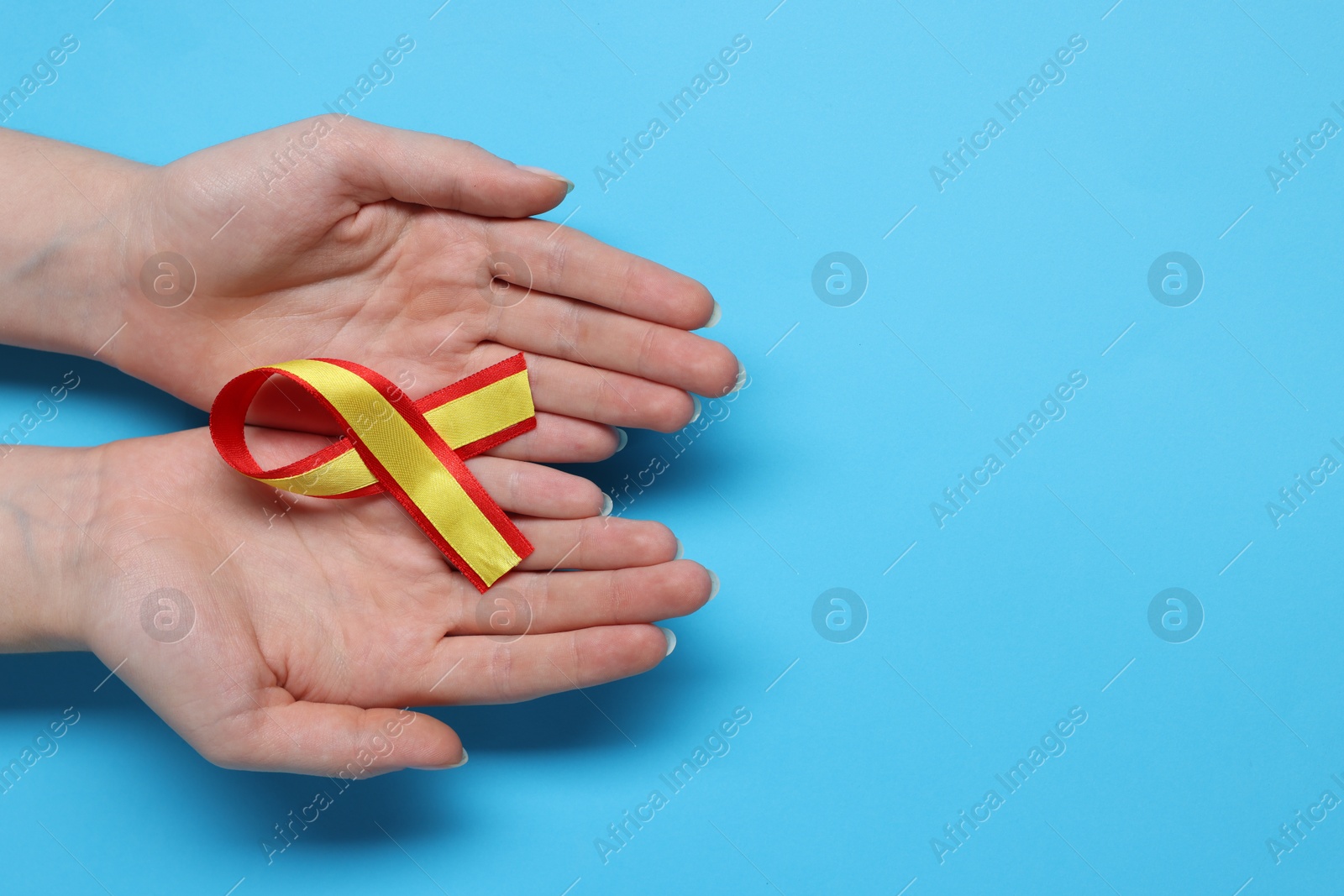 Photo of Woman with yellow and red ribbon on light blue background, top view with space for text. Hepatitis C awareness