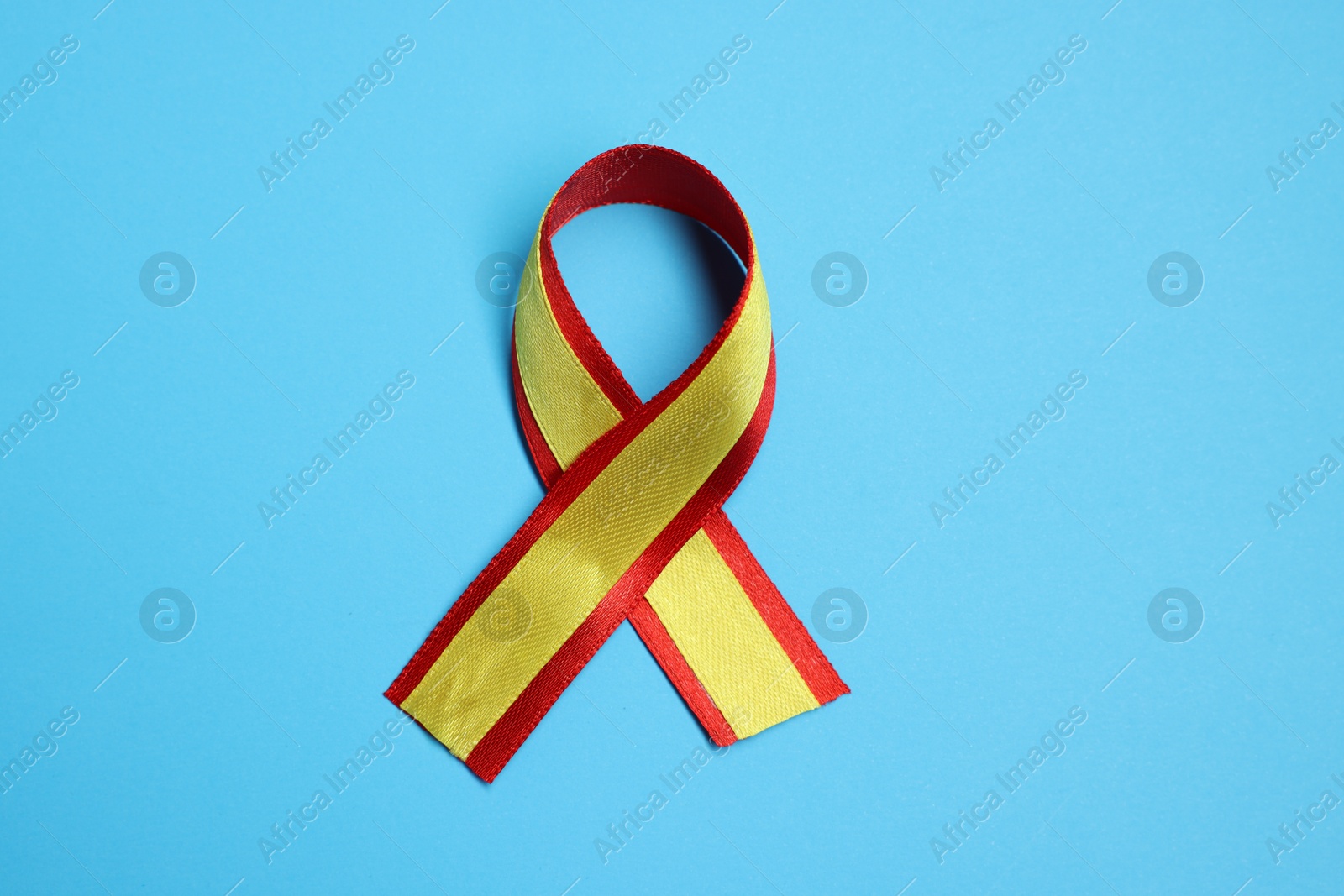 Photo of One yellow and red ribbon on light blue background, top view. Hepatitis C awareness