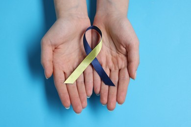 Woman with colorful ribbon on light blue background, top view. Down syndrome awareness