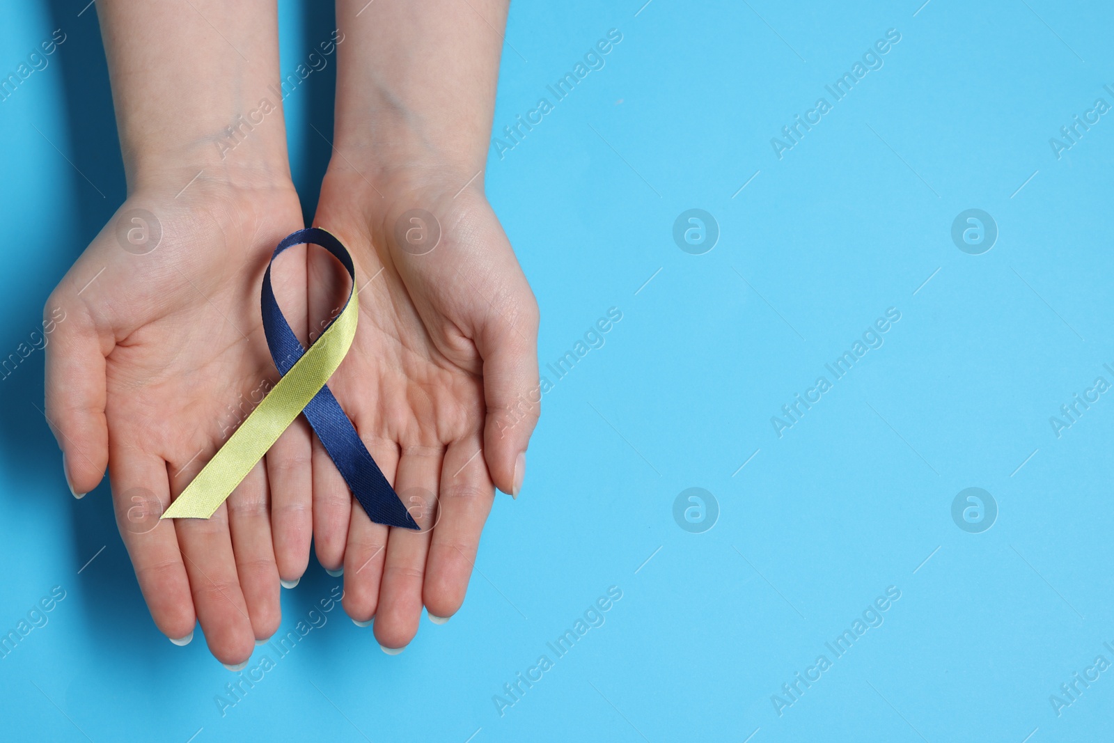 Photo of Woman with colorful ribbon on light blue background, top view and space for text. Down syndrome awareness