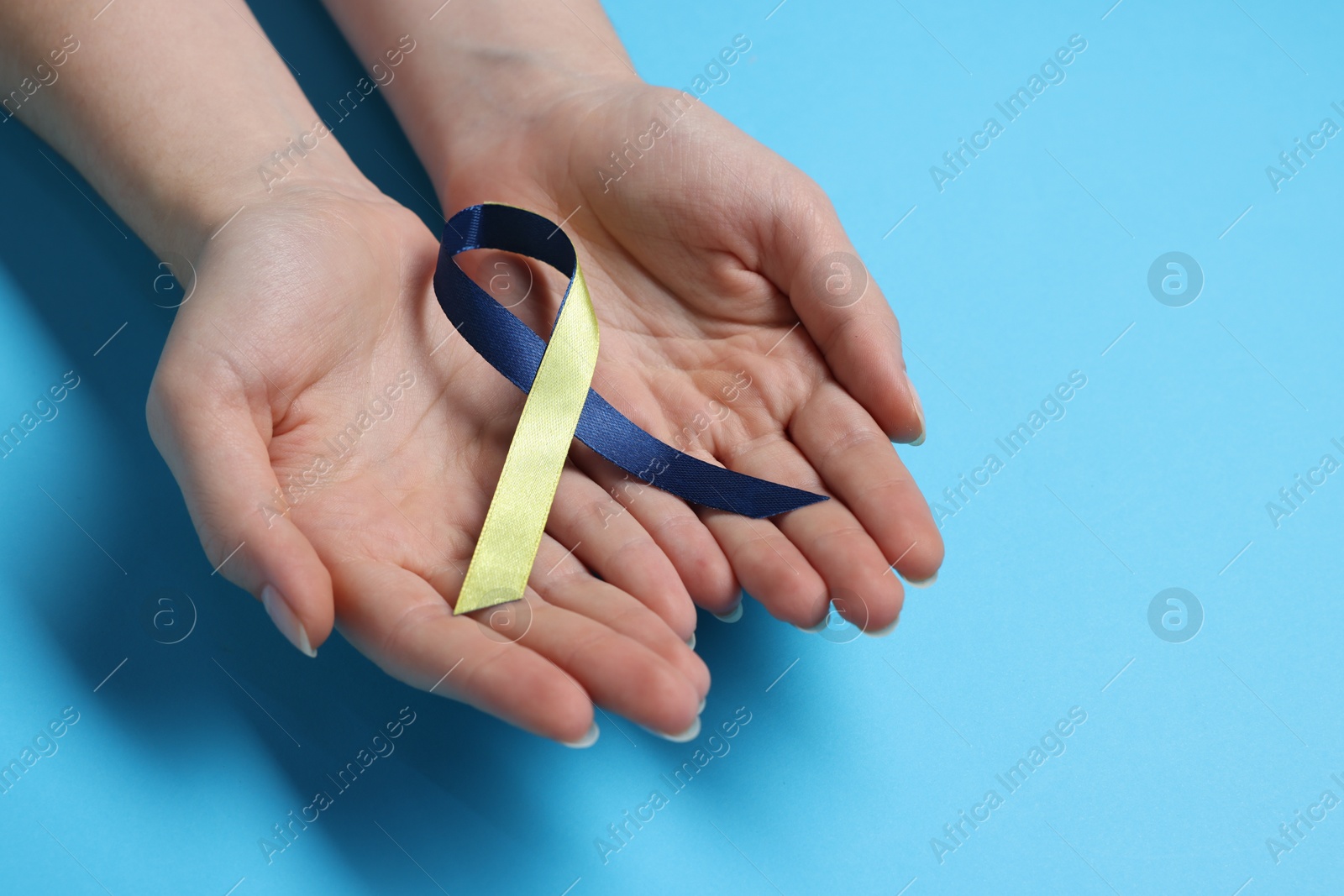 Photo of Woman with colorful ribbon on light blue background, closeup. Down syndrome awareness