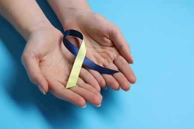 Photo of Woman with colorful ribbon on light blue background, closeup. Down syndrome awareness