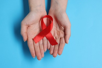 Photo of Woman with red ribbon on light blue background, top view. HIV (AIDS) disease awareness