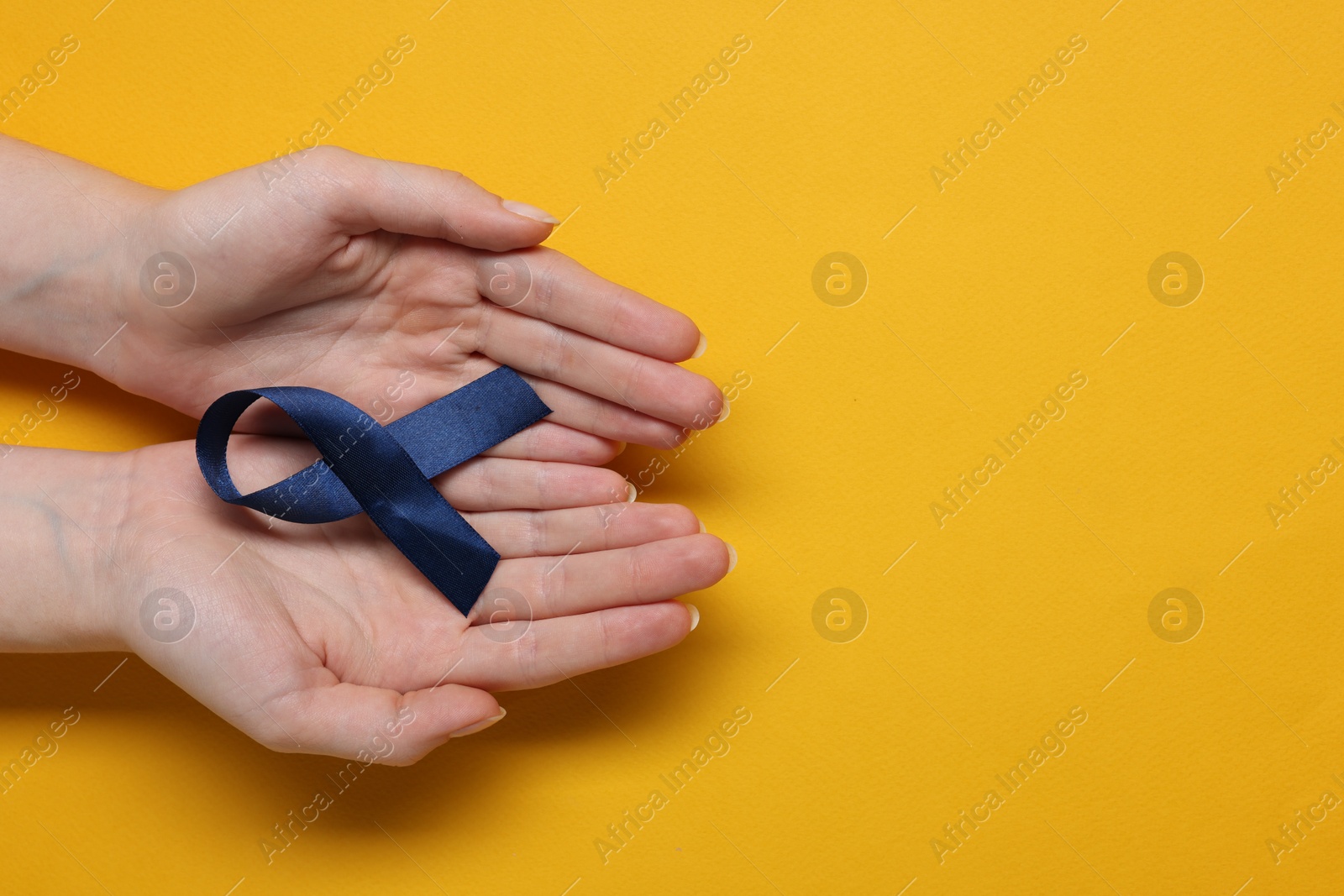 Photo of Woman with dark blue ribbon on yellow background, top view with space for text. Arthritis disease and colon cancer awareness