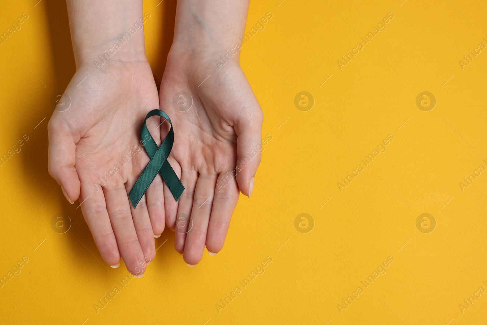 Photo of Woman with teal ribbon on yellow background, top view with space for text. Ovarian cancer and gynecological disorders awareness