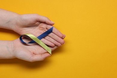 Photo of Woman with colorful ribbon on yellow background, top view and space for text. Down syndrome awareness