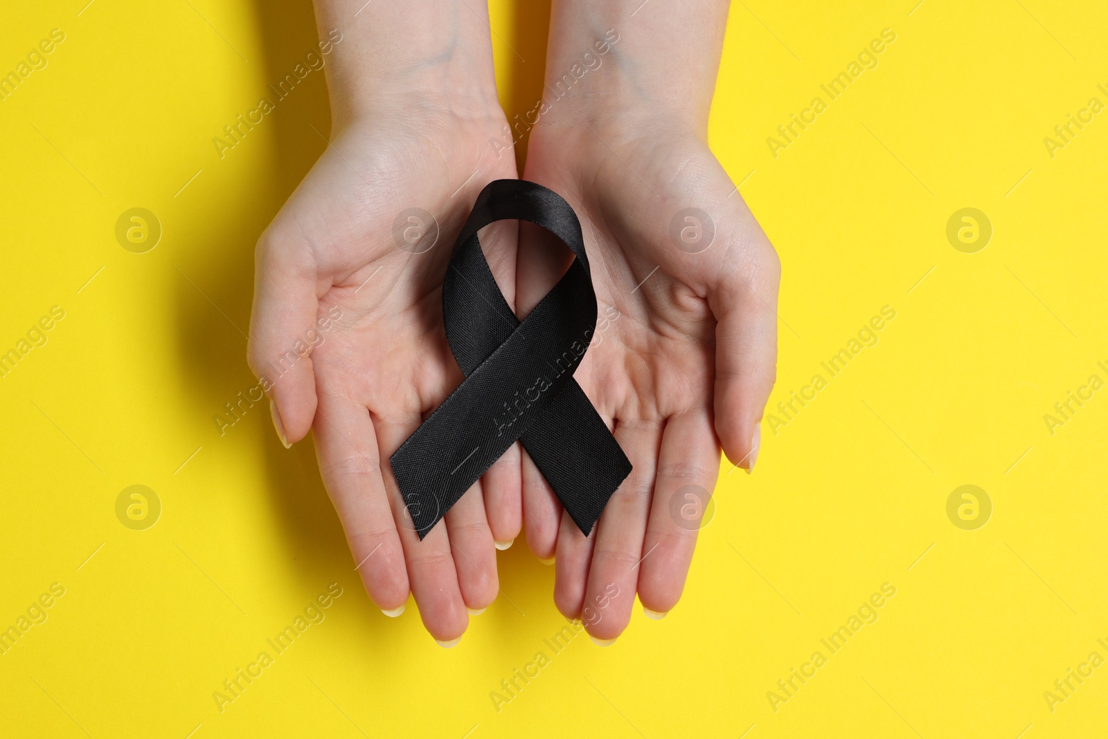 Photo of Woman with black ribbon on yellow background, top view. Melanoma and mourning concept