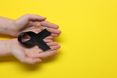 Photo of Woman with black ribbon on yellow background, top view with space for text. Melanoma and mourning concept